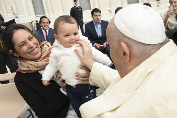 pope francis faces away from the camera, blessing a smiling baby in a white fuzzy coat
