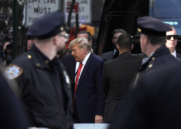 Donald Trump, with bowed head, arrives to Trump Tower surrounded by police officers following his indictment in New York City.