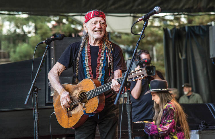 A smiling Willie Nelson playing his guitar Trigger at a recent concert. 