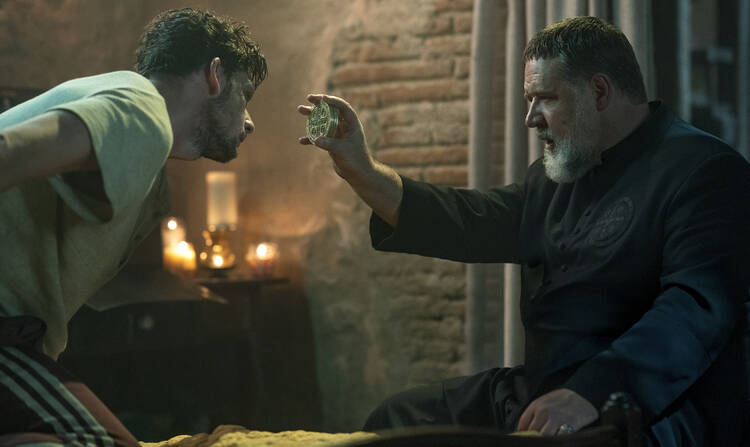 russell crowe as father amorth blesses a man who is possessed by a demon with a small icon in his hand, the scene is dark with candles lit behind the two characters in the movie still