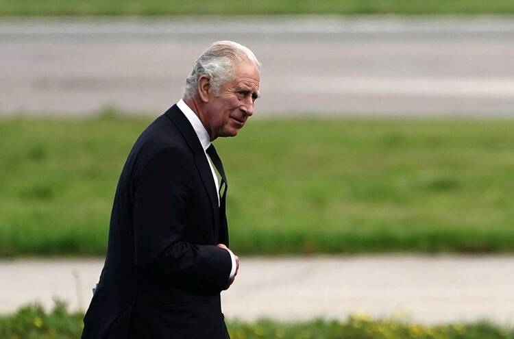 king charles walks wearing a dark suit with green grass behind him