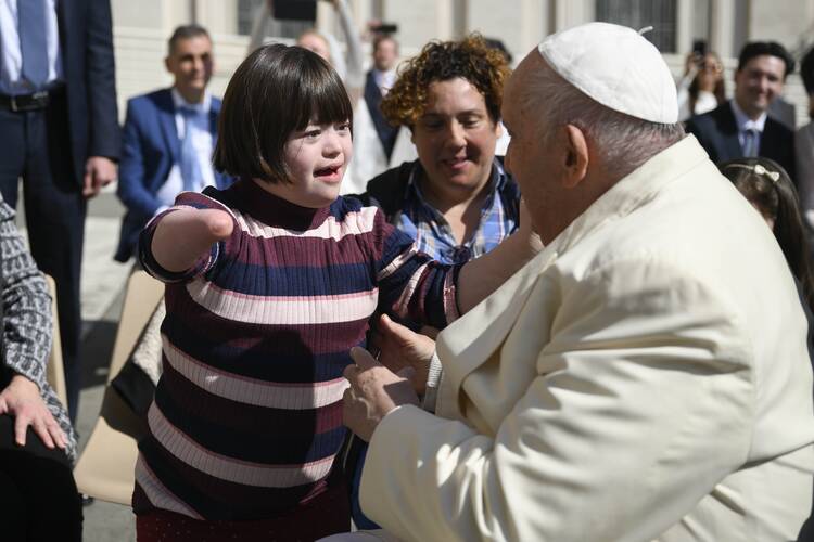a child reaches out to hug pope francis, the child wears a pink and purple striped shirt and is missing most of an arm, pope francis is turned away from the camera to hug her