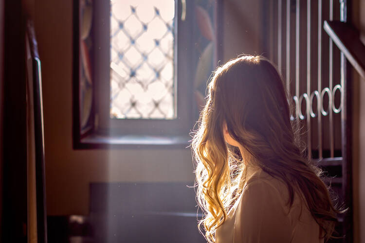Teen girl sits alone in a church looking through a stained glass window