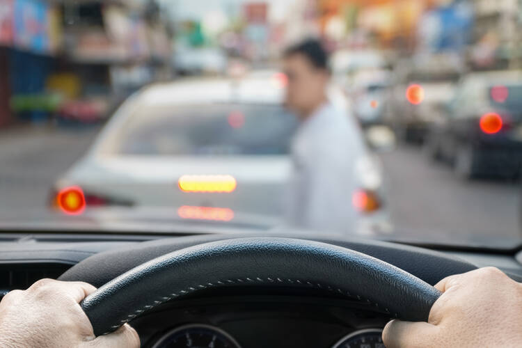 A blurry image of a pedestrian is seen behind a car's steering wheel and through a windshield.