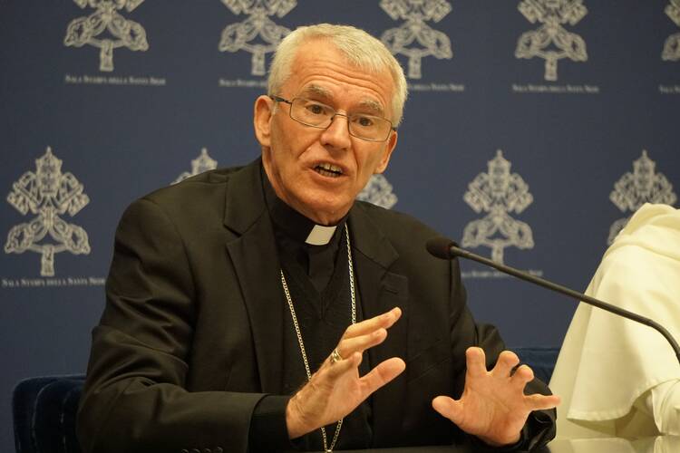 A priest in a Roman collar speaks into a mic