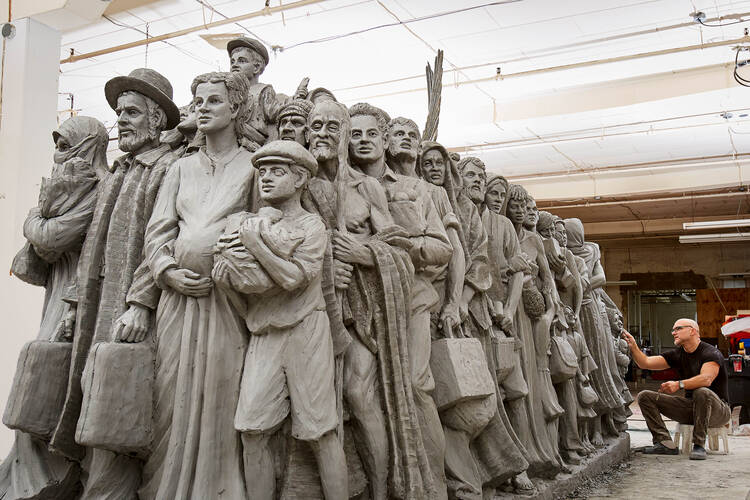 a sculpture with a lot of people, immigrants and people of color, with scared or hopeful faces; an angel's wings peak up in the midst of them