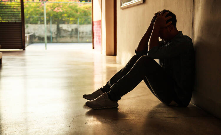 a young man in shadow sits with his head in his hands in an empty hallway