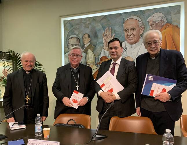 Three Catholic priests and a man in a suit pose for a photo