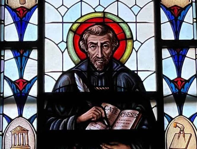a stained glass image of st peter canisius with a red halo and writing in a book