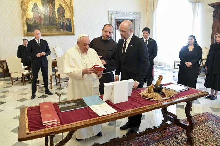 The Pope and a politician stand in front of a table with gifts on it