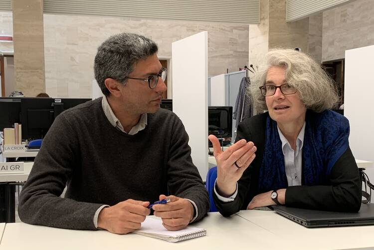 sr nathalie becquart speaks to a male journalist sitting at a table, sr nathalie gesture with her hand and the journalist watches as she speaks, taking notes