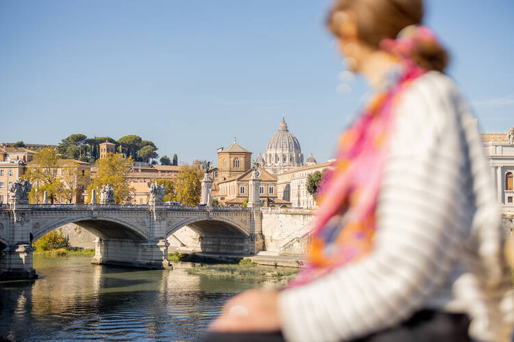 a blurry young woman in a scarf sits on a bridge and looks at st peters basilica in the distance 