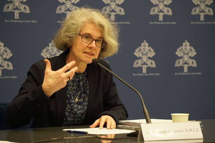 a woman with grey hair and glasses speaks into a microphone at the vatican