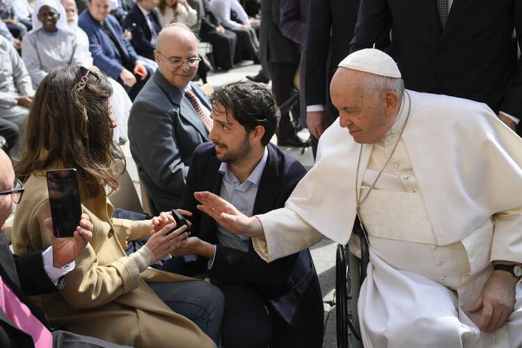 a man kneels before his girlfriend proposing marriage as the pope sits next to them and blesses them