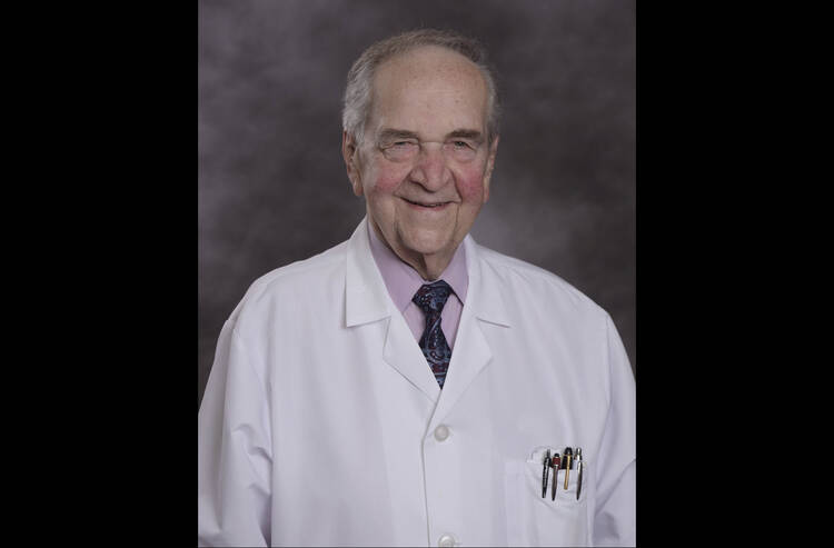 a man with grey hair in a white medical coat poses for a headshot