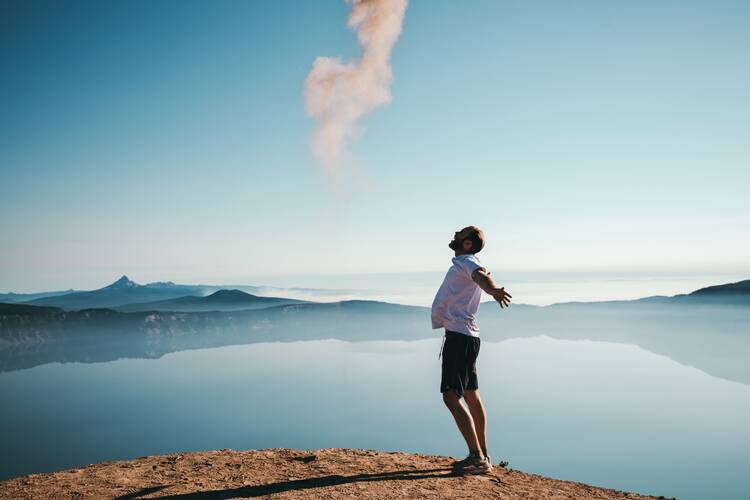 Man standing on sand while spreading arms beside calm body of water