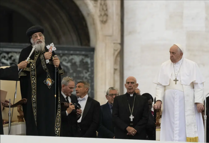 Roman Catholic and Coptic Orthodox priests stand on a stage 