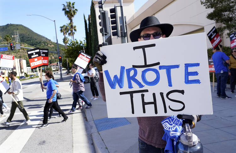 Justice Hardy, a writer on the television series "True Lies," holds up a sign as members of The Writers Guild of America picket outside Warner Bros. Studios, on May 2, 2023, in Burbank, Calif. The use of ChatGPT is as controversial in the entertainment industry as it is in schools. (AP Photo/Chris Pizzello)