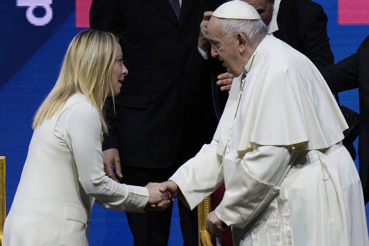 pope francis at right shakes the hand of giorgia meloni at left, both are wearing white clothes in front of a dark background