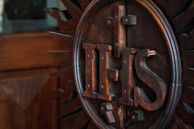 the ihs logo of the jesuits carved and with a wooden background