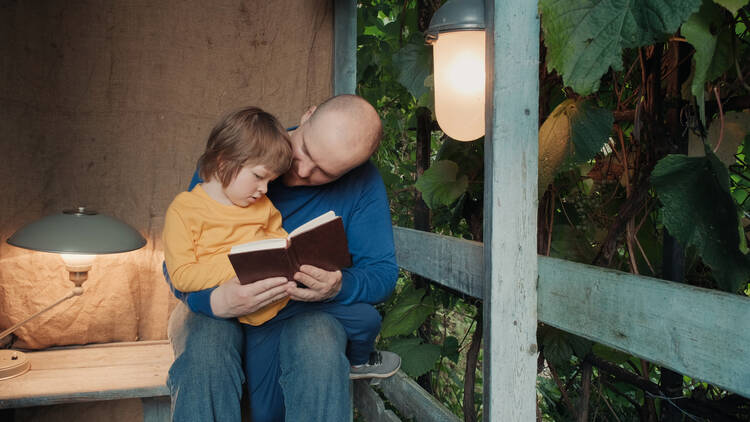 A man reads to a toddler sitting on his lap on a porch