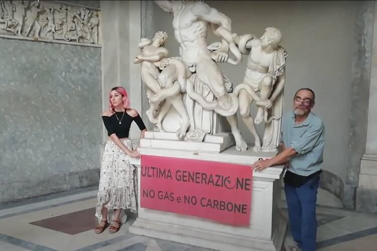 An Italian man and woman stand with a climate change banner in front of a sculpture