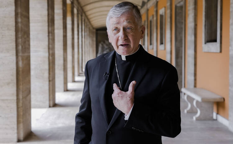 Cardinal Blase Cupich points to himself in outdoor hallway in Rome, Italy.