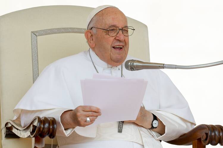 pope francis speaks from his chair at the general audience, he gestures with his hand and smiles as he talks