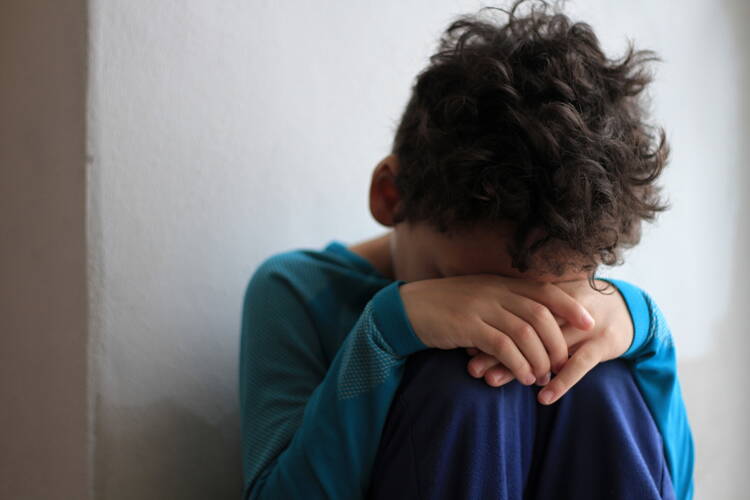 A child sits against a wall and covers his face with his hands (iStock)