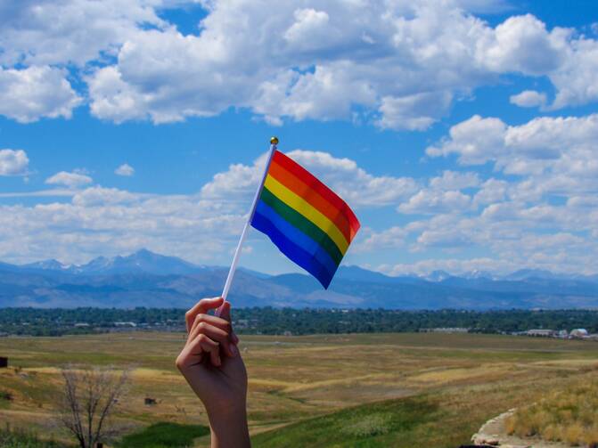 Pride flag against a background of mountains and blue sky.