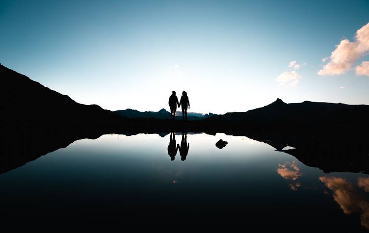 Silhouette of people holding hands in front of body of water