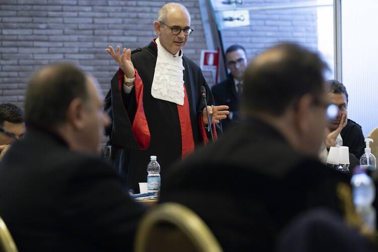 alessandro diddi stands in a crowd of people, he wears black with a white collar and some red tassels