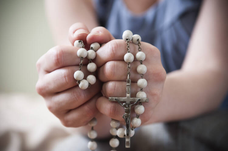 A close-up of a young woman's hands holding a white rosary. (iStock/magnez2)
