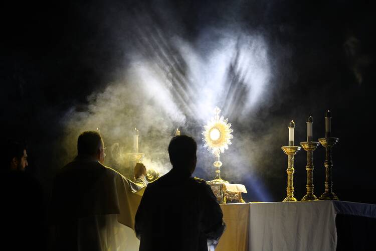 people kneel in front of a monstrance with light shining on it from above