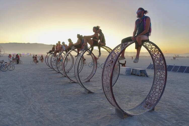 Men and women siting on large wheels in the desert at sunset at the Burning Man festival