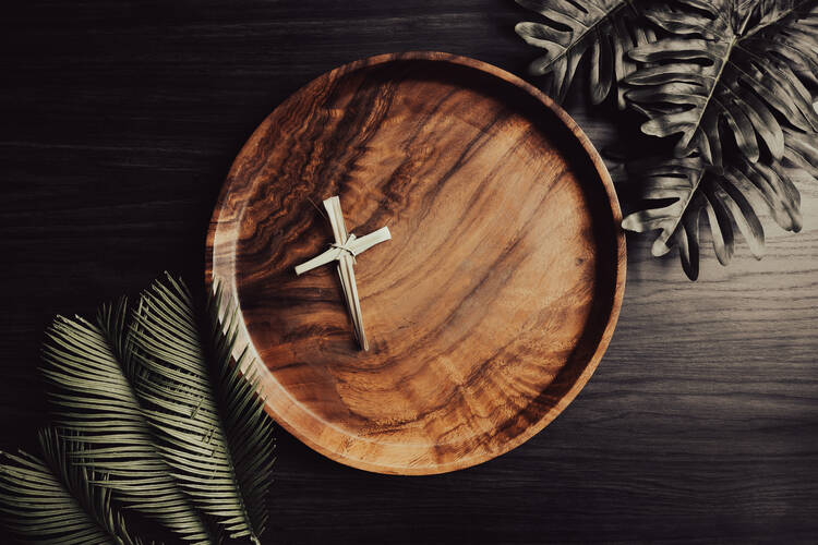 A dried palm cross on an otherwise empty circular teak plate surrounded by palms 