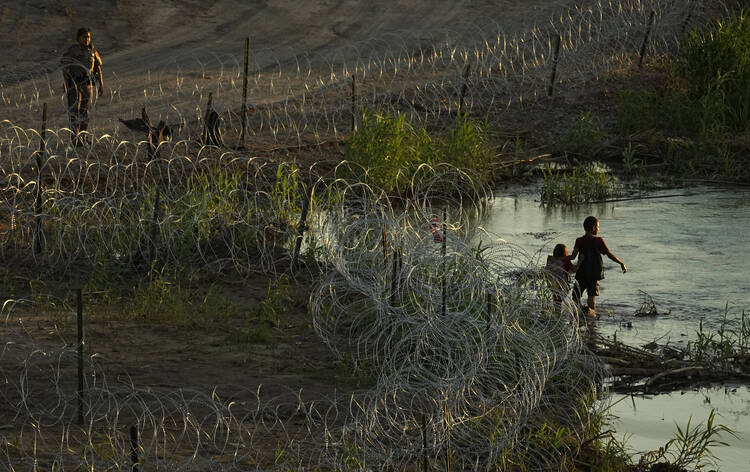 Migrants walk along concertina wire as they try to cross the Rio Grande at the Texas-U.S. border in Eagle Pass, Texas, Thursday, July 6, 2023. (AP Photo/Eric Gay)