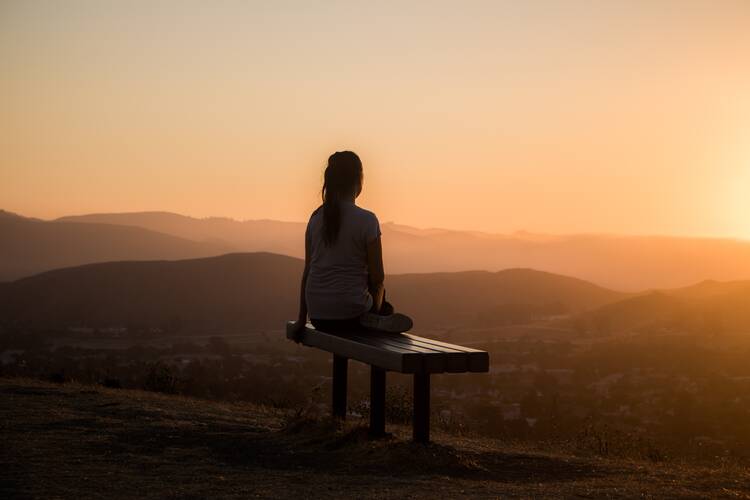 woman sitting on bench looking over mountains