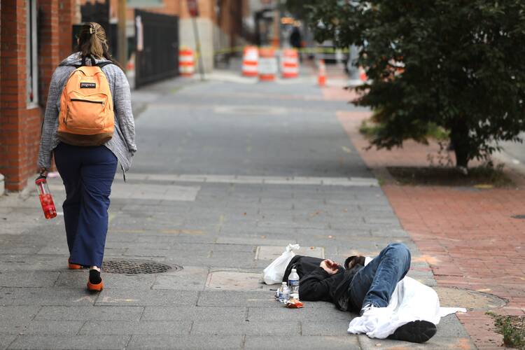 A woman walks past a man sleeping on a sidewalk in Baltimore on June 6, 2023. (OSV News photo/Bob Roller)