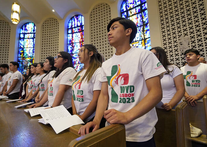 Young people stand in church pews wearing shirts that say WYD Lisbon 2023.