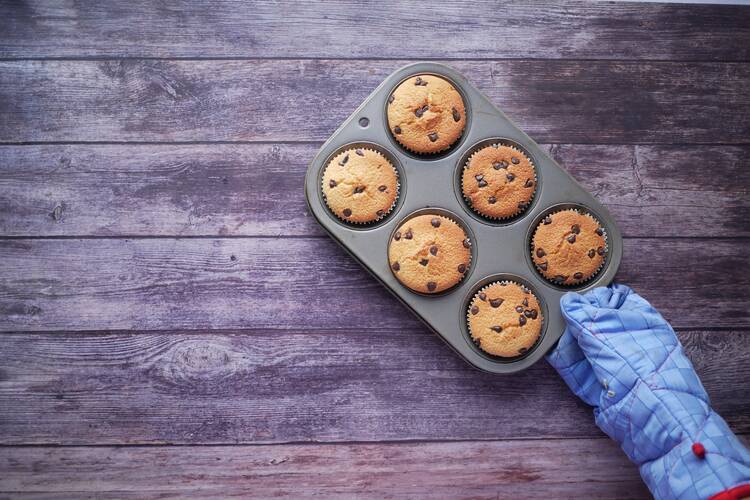 Muffins in a muffin tin, being held by a hand in an oven mitt