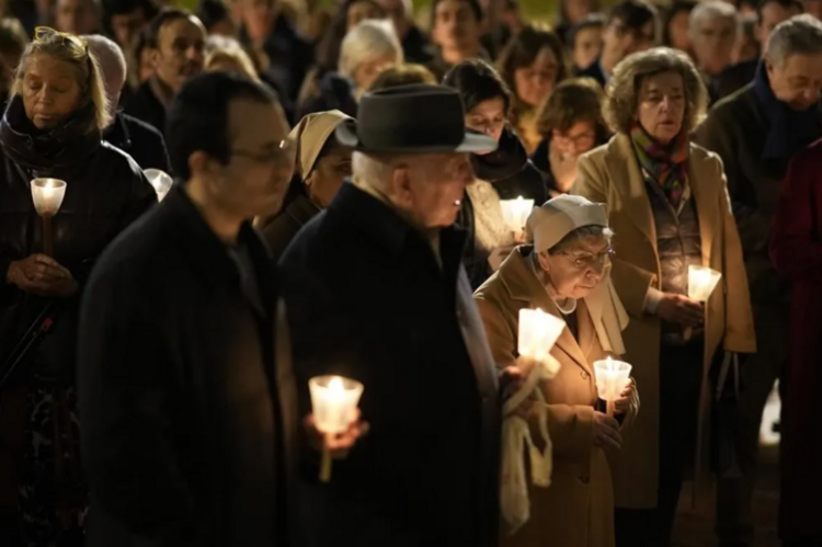 People in coats hold candles at a vigil in Lisbon. 