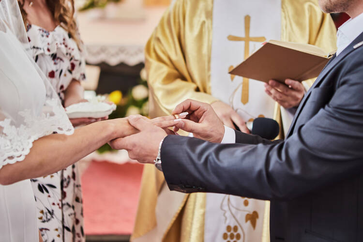 A close-up of a Catholic wedding ceremony, focusing on the hands of the bride, groom and priest.