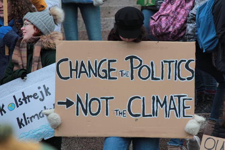 A kid holds a sign that says "change politics not the climate"