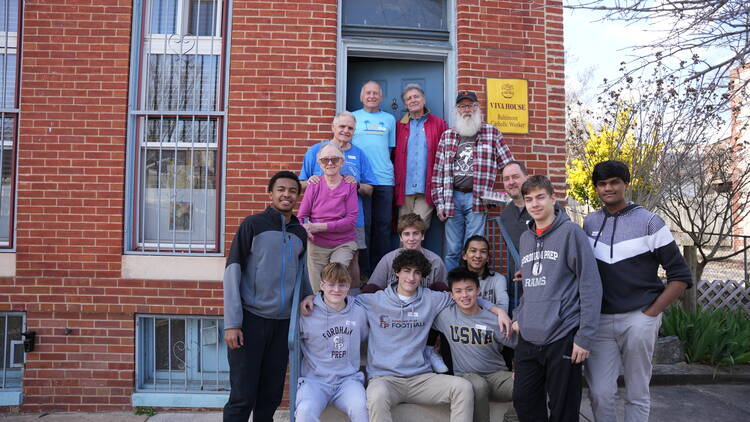 Students from Fordham Prep and other Viva House volunteers join Brendan Walsh, at left in dark blue shirt, and his wife Willa Bickham, standing below, on the steps of Viva House in Baltimore, Md., in March 2023.
