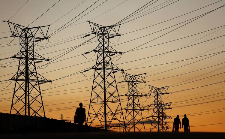 People in Soweto, South Africa, walk past electricity pylons July 3, 2022, during frequent power outages because of aging coal-fired plants. (CNS photo/Siphiwe Sibeko, Reuters)