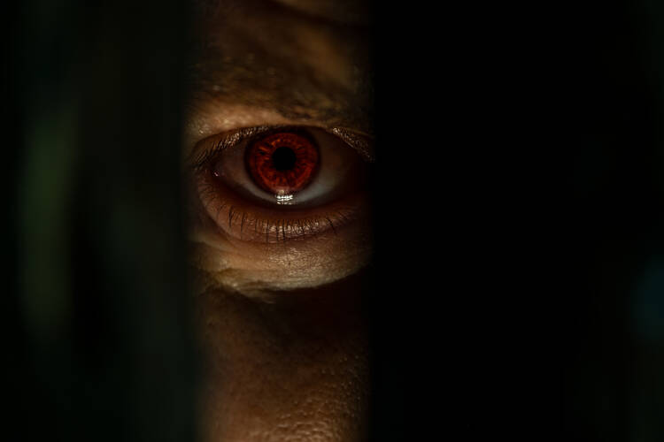 A photo of a red eyeball, with a face shrouded in darkness