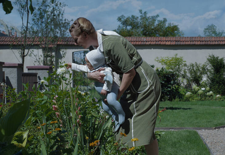 The actress Sandra Hüller holding a baby in a garden in a scene from the film “The Zone of Interest”