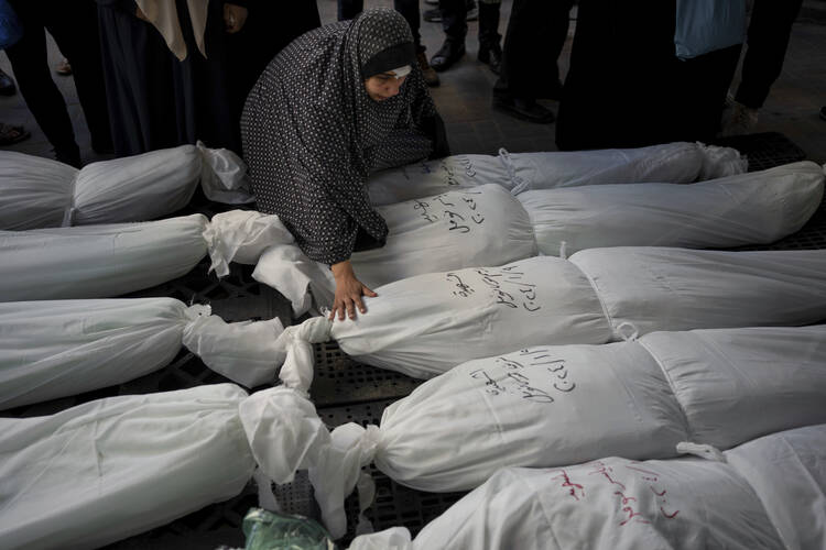 A woman walks through rows of white-wrapped bodies, touching one, as Palestinians mourn their relatives killed in the Israeli bombardment of the Gaza Strip, outside a morgue in Rafah, southern Gaza, Wednesday, Jan. 10, 2024. (AP Photo/Fatima Shbair)