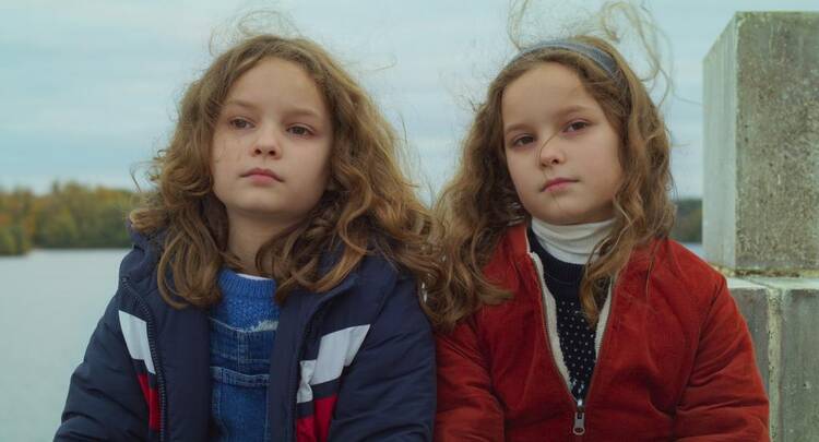 An image from the film Petite Maman of two sisters sitting next to each other in winter jackets